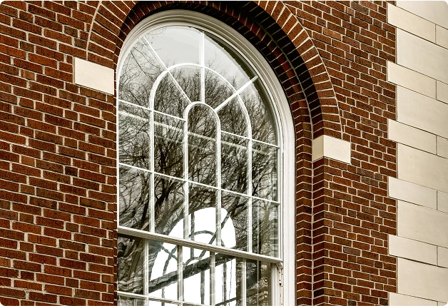 Exterior view of an arched, white-framed window with WindowSLIP installed, set in a red brick wall.