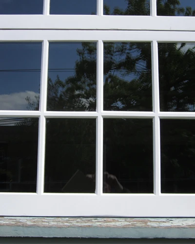 Exterior view of a white-framed grid window without WindowSLIP installed, set in a worn wooden frame.