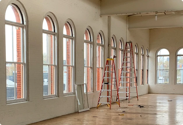 Spacious room with arched windows undergoing WindowSLIP installation, featuring wood floors and ladders set up near the windows.