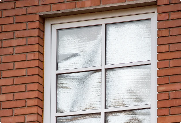 White-framed window with foil applied to panes for insulation and heat reflection, set in a red brick wall.
