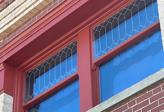 Red-framed window with geometric glass and WindowSLIP installed, set in a red and light brick facade.