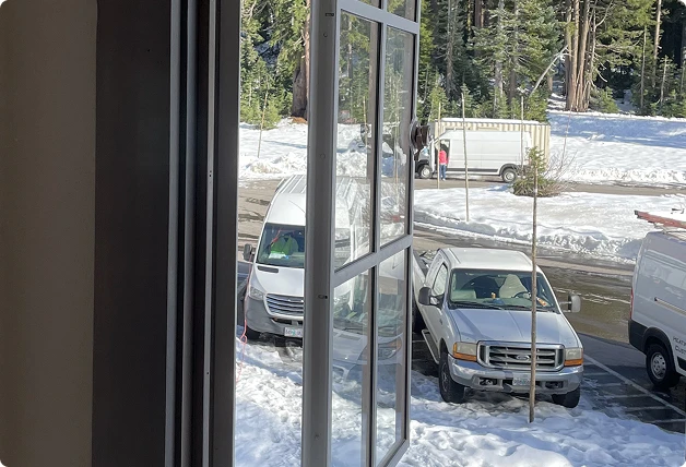 Interior view of an open WindowSLIP insert in a wooden window frame, looking out onto a snowy landscape with parked vehicles.