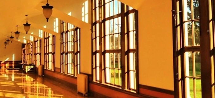 Sunlit hallway with large windows featuring WindowSLIP installed, casting reflections on a polished wooden floor.