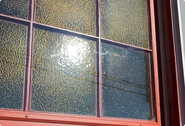 charts_shutterstock_2440357647 3 Close-up of a red-framed window with textured glass reflecting sunlight, set in a red brick wall.