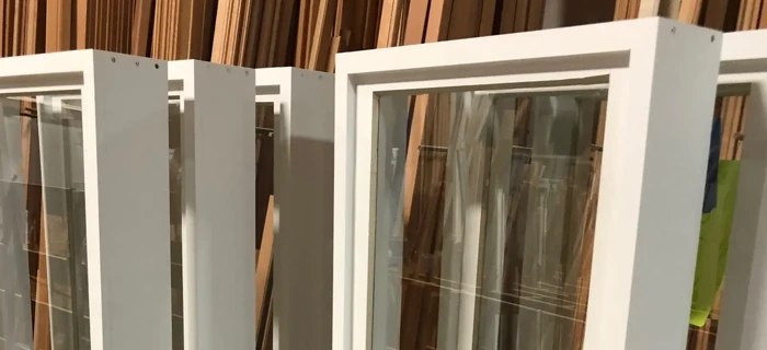 White-framed glass windows stacked on a concrete floor in a storage area with wooden beams visible in the background.